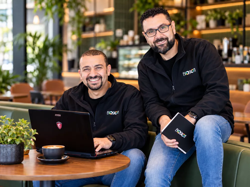Nadir and Marten in their Evosion jackets at a café table